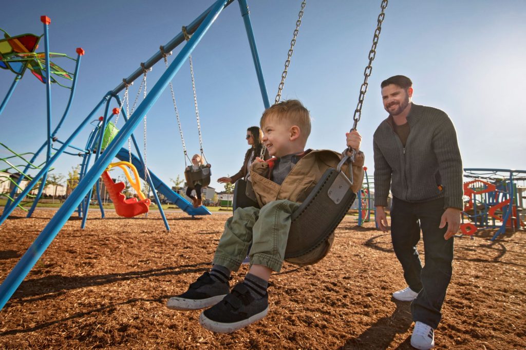 A father pushing a young child on a playground swing