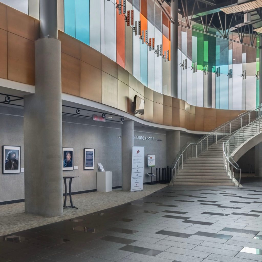 Interior of a theatre lobby, with a curved staircase and a wall of posters