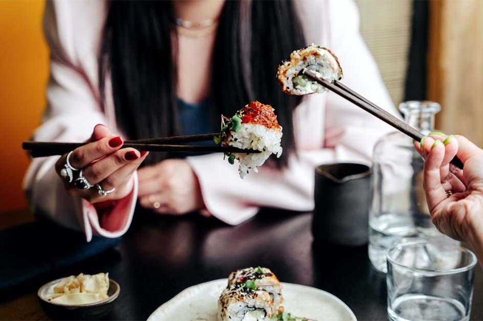 A diner lifting a piece of sushi with chopsticks