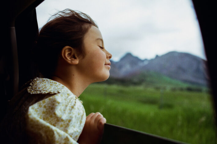 A child leaning out of a car window with her eyes closed