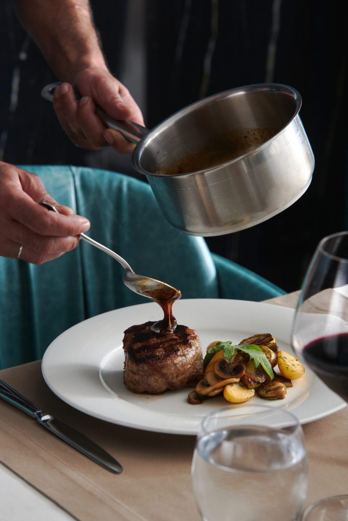 A chef spooning sauce over a plated steak