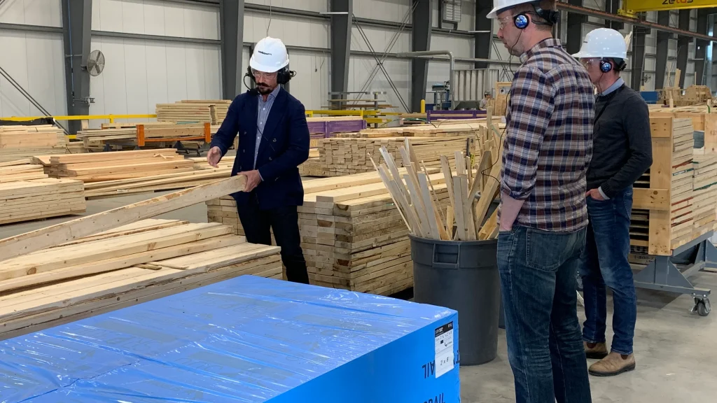 Visitors in hard hats being shown stacked timber on the factory floor