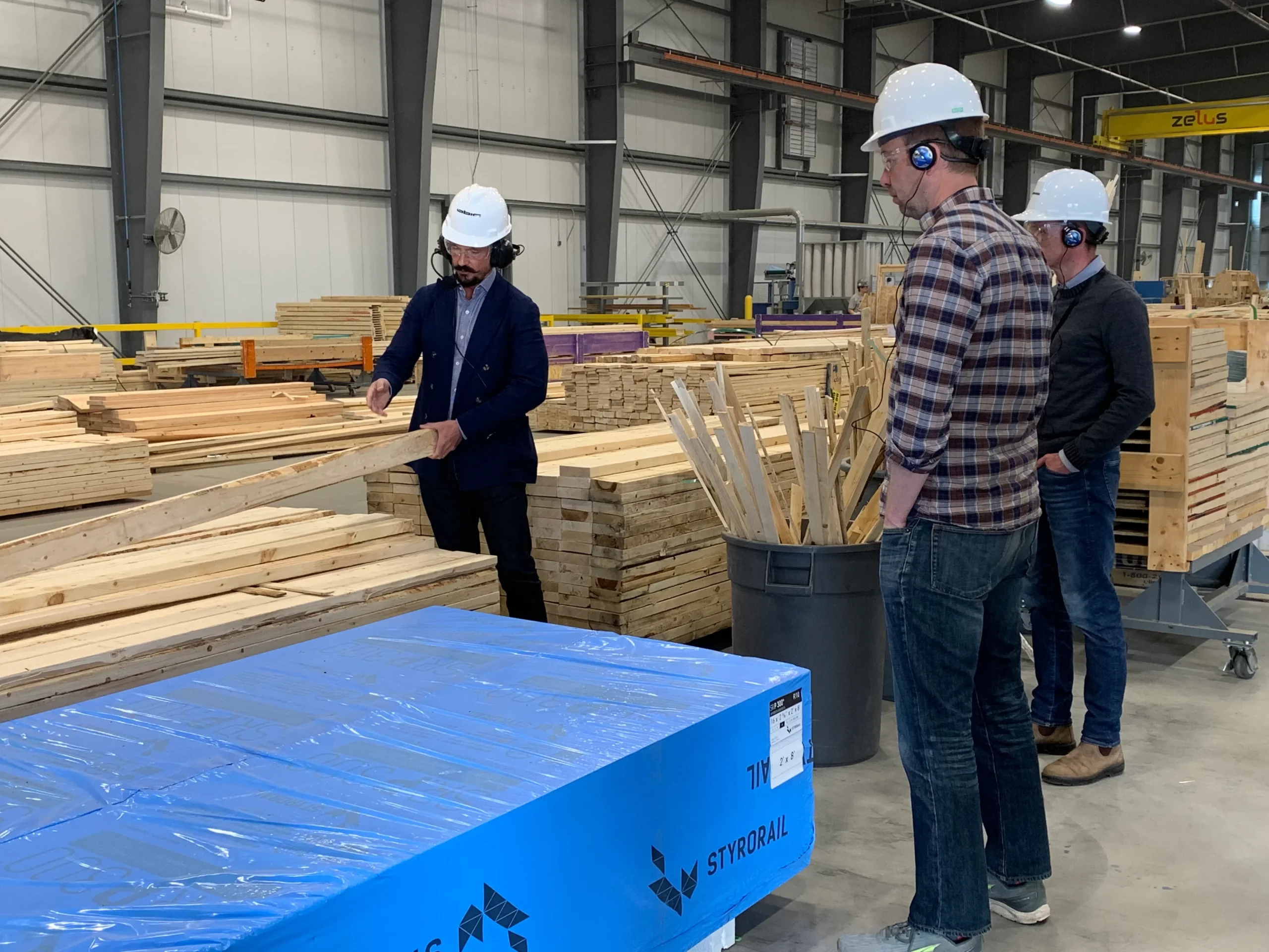 Visitors in hard hats being shown stacked timber on the factory floor