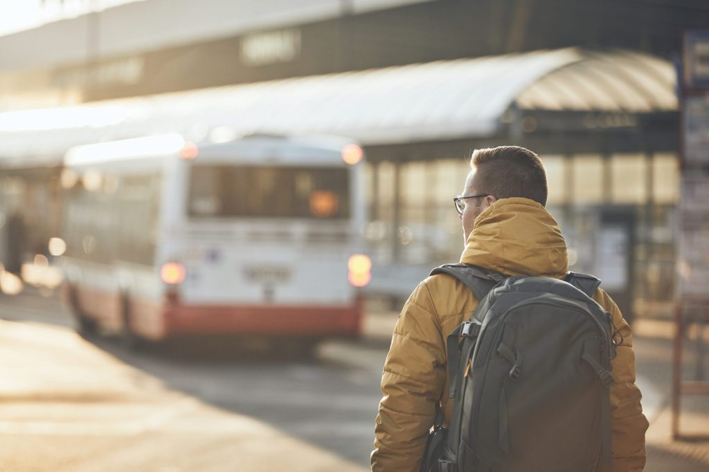 A passenger with a backpack waiting as a bus pulls into a transit station