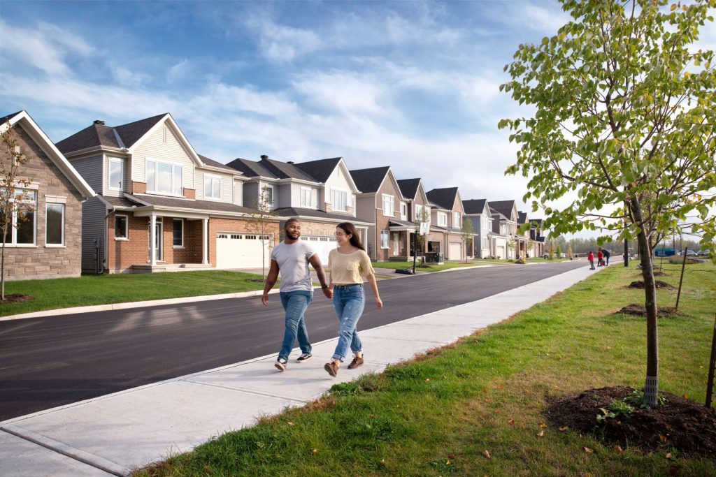 Two people walking a path beside a street of Orléans Village homes