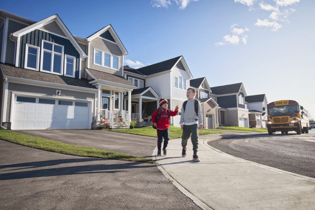 Two children walking home past Orléans Village homes, with a school bus behind