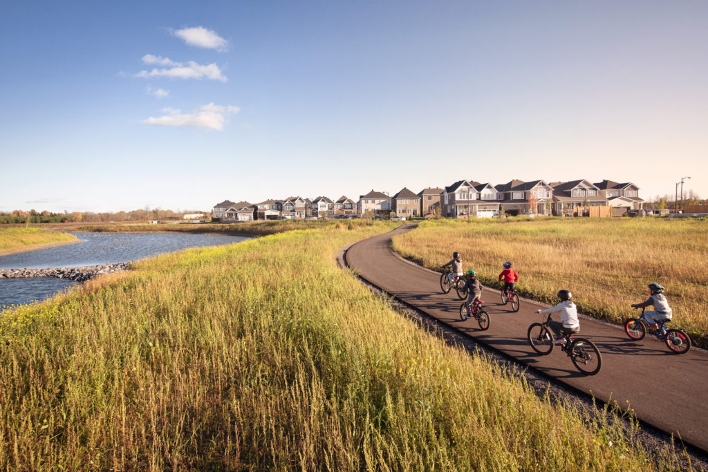 Children cycling a path beside the Fox Run community pond, with homes on the ridge behind